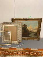 Group shot of large gilt-framed painting, two silver ornate frames, and one simple wood frame