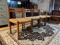 Four teak chairs arranged in line on patterned rug, showing overall set