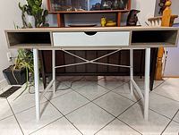 Front view of desk showing woodgrain surface, white legs and drawer with open shelves.