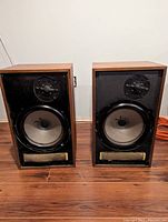 Front view of both speakers with grilles removed, showing drivers and port grilles.