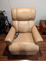 Front view of beige leather power recliner with remote on seat.