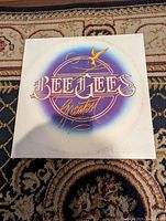 Front cover of Bee Gees Greatest vinyl record album showing purple and gold logo on white background.