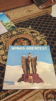 Front cover of Wings Greatest album showing statue figure in desert landscape.