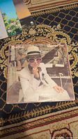 Front cover of Elton John Greatest Hits vinyl album showing Elton John in white suit and hat at piano.