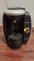 Front view of the Bosch Tassimo coffee maker with the drip tray in place, illuminated dial showing the machine powered on.