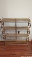 Front view of vintage metal 4-tier bookshelf showing open wire grid shelves and gold finish.