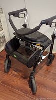 Front angle of folding walker showing the padded seat, front mesh basket, and wheels