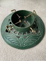Top view showing the round green cast iron Christmas tree stand with four metal screwed clamps with triangular handles.