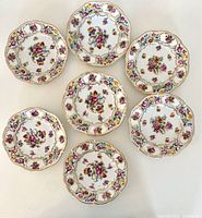 Seven reticulated Dresden floral porcelain plates arranged in a circle showing the colorful floral designs and gold edging.