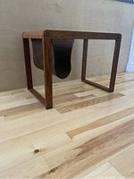 Mid century magazine table with wooden rectangular frame and dark brown faux leather sling holder. View shows the table structure and sling hanging inside.