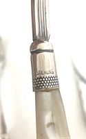 Close-up photo showing the sterling silver marking on the cuff of a mother of pearl handle on one of the knives