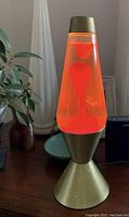 Photo showing the Astro lava lamp glowing with red wax inside a yellow/orange liquid. Brass-colored base and cap visible.