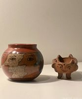 Overall view of the two redware pottery vessels: the round painted jar and the small sculpted footed dish with face design.