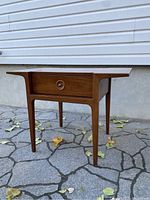 Side view of the walnut side table showing tapered legs and drawer with circular knob.
