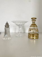 Photo of Stuart crystal comport, sugar caster, and vintage glass decanter together on a shelf.