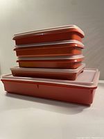 Stacked view of five vintage Tupperware deli/meat keepers in paprika and white lids.