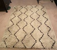 Photo of rectangular cream shag carpet with dark zig-zag Wazuu pattern, showing overall condition and pile texture.