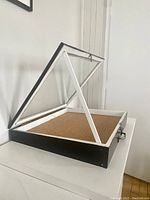 Angled side view of the wood framed glass display case with cork base, latch, and metal support prop holding lid open.