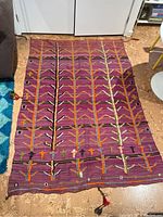 Full view of purple Moroccan area rug with colorfully stitched tree pattern, tassels at corners, and fringe at one end