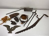 Photo showing full lot of primitive cast iron tools and decorative items arranged on white surface.