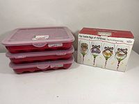 Three stacked red Sterilite ornament storage trays with clear lids, used for storing holiday ornaments safely.