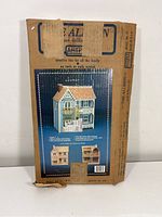 Box front showing Artply The Allison wood dollhouse kit with blue dollhouse image, model number 77, with markings and tape on cardboard box.