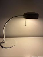 White Ledu contemporary cantilevered metal desk lamp lit, shown from a slight side angle to highlight lamp shape and shade.