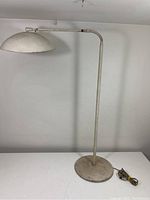 Full view of mid-century modern floor lamp showing curved arm, dome-shaped shade, round flat base, and visible paint wear/rust.