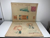 Two large vintage architectural drawings displayed one above the other on the floor. The top drawing shows multiple views and floor plans for a city church with blue-green accents; the bottom drawing features exhibition building plans with circular and linear forms.