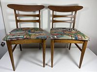 Pair of vintage mid century dining chairs with vibrant upholstery featuring Route 66 and road trip imagery, set on a white background to show condition and style.