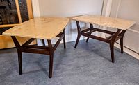 Two mid-century style side tables with cream marble tops and wooden bases shown at angle.