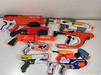 Photo showing the full set of 11 Nerf blasters arranged on white surface, visible various models including Rival and Fortnite series.
