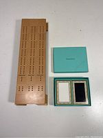 Wooden cribbage board and Tiffany & Co playing cards with original box displayed on white surface.