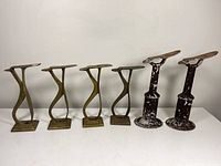 Front view of four brass and two cast iron shoe shine stands arranged in a row on a white table against a white background.