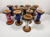Front view of all 13 wooden spools showing various yarns and ribbons in multiple colors.