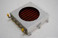 Aluminum heat exchanger with circular red finned cooling area and yellow capped inlet/outlet fittings on side.