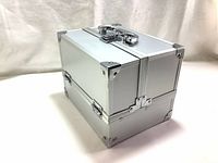 Front and side angle of the closed silver aluminum makeup train case showing metal handle and latch, corner protectors.