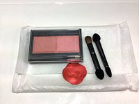 Full lot showing blush duo palette, two mini double-ended eyeshadow brushes and red flower accessory on white tissue paper.