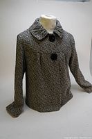 Front angled view of the black and white tweed jacket on a mannequin, showing collar, sleeves, and buttons.