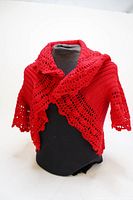 Front view of red crochet vest on black mannequin showing shawl collar and lace crochet edges on sleeves and hem.