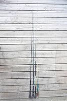 Four vintage fishing rods laid side by side showing different handle colors and rod lengths against a wooden deck