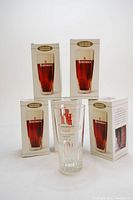 Six boxes of Rodenbach beer glasses with one glass removed and standing in front showing clear glass with red Rodenbach logo and faceted base.