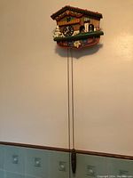 Full view of the German cuckoo clock wall mounted with one pine cone weight hanging and one weight missing.