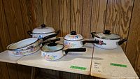 Full view of cookware set on table showing five enamel pieces with colorful floral patterns and black handles and knobs.