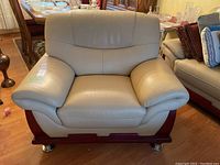 Front view of beige leather armchair showing wood trim base and metal feet on hardwood floor near dining area.