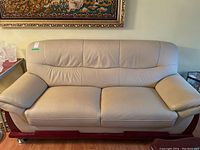 Front view of the two-seat beige leather sofa showing wood trim base and metal legs