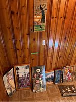 Assortment of framed paper prints under glass leaning against wood panel wall and woven scroll print hung above