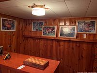 Photo of five framed prints on wood-paneled walls above a table with a chessboard, showing the variety and framing style.