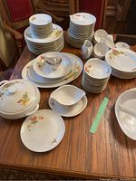 Full set of Polish china pieces arranged on wooden table showing plates, bowls, cups, saucers, and serving items with floral and gold trim design.