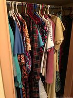 Assortment of approximately 15 vintage women's garments hanging on a rod, including dresses, tops, coats in various prints and colors